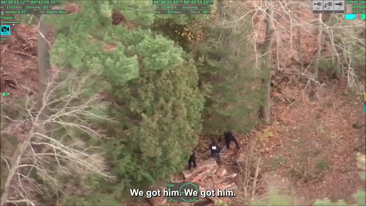 Aerial view of a wooded swamp area near a country club, with law enforcement personnel searching for an escapee.